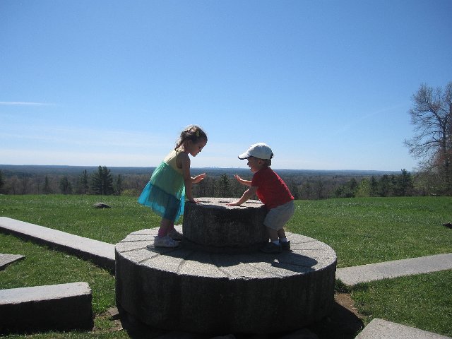 IMG_9232.jpg - A gorgeous day atop Holt Hill.  It looks like Nathan is about to eat the Boston Skyline.  The kids, of course, are playing drums on the solstice stones.
